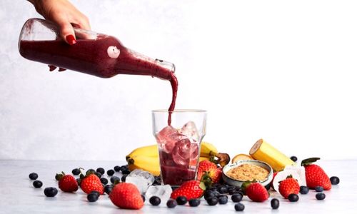 Image of red smoothie being poured into a class surrounded by berries