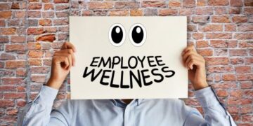 Image of a person against a brick wall holding a sign over their head with eyes and the smile replaced with employee wellness
